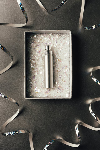 top view of perfume bottle in box and shiny silver ribbons on grey